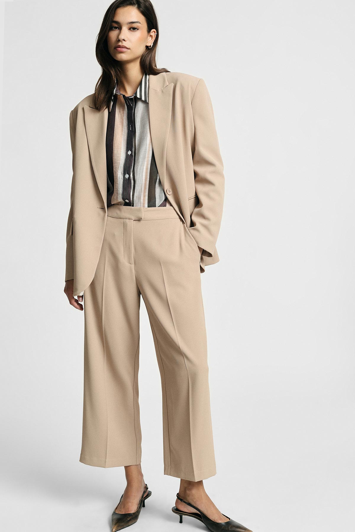 Woman wearing beige tailored blazer and wide-leg trousers with striped button-up shirt and black slingback heels