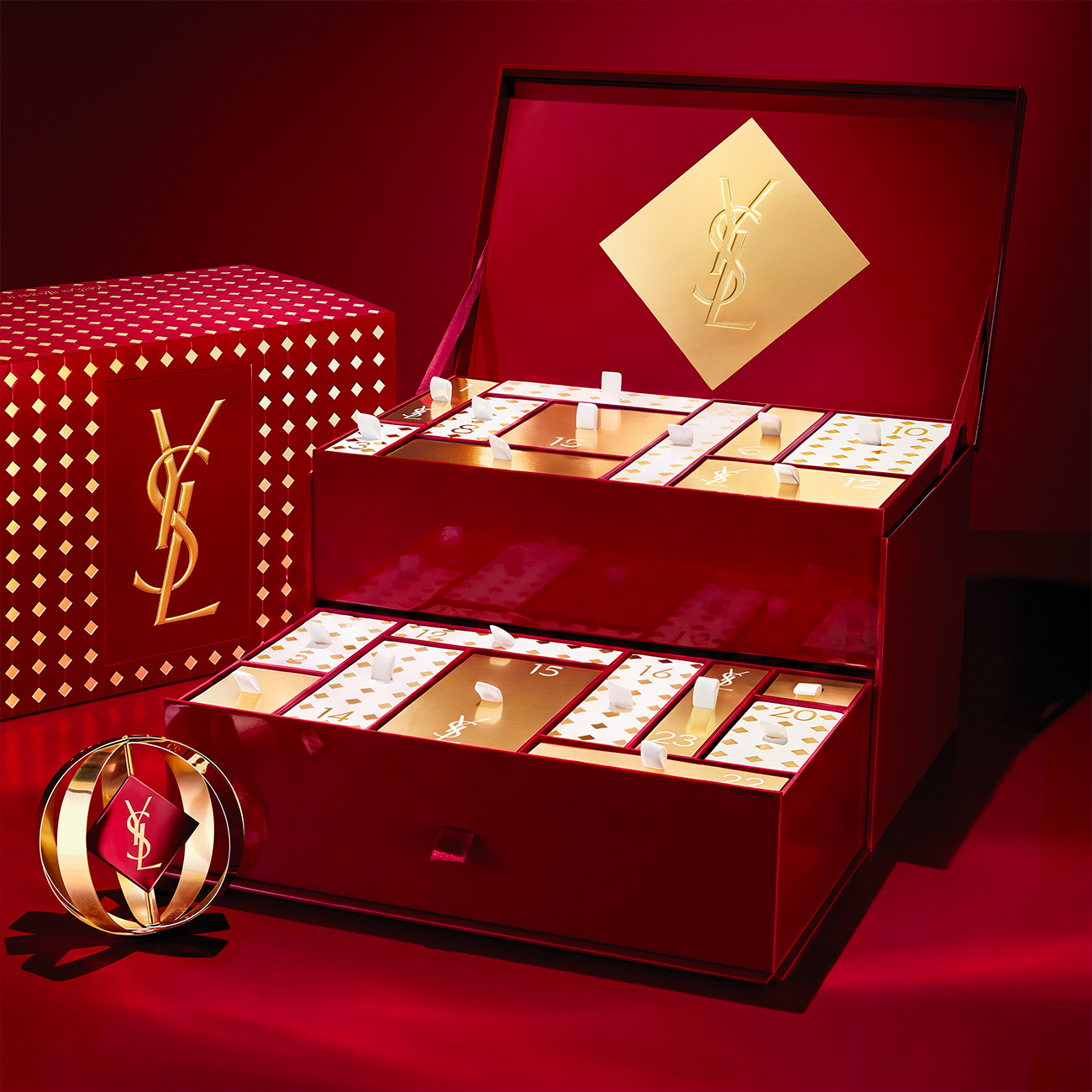 Un lussuoso calendario dell'Avvento YSL rosso e oro aperto con cassetti e scomparti numerati.