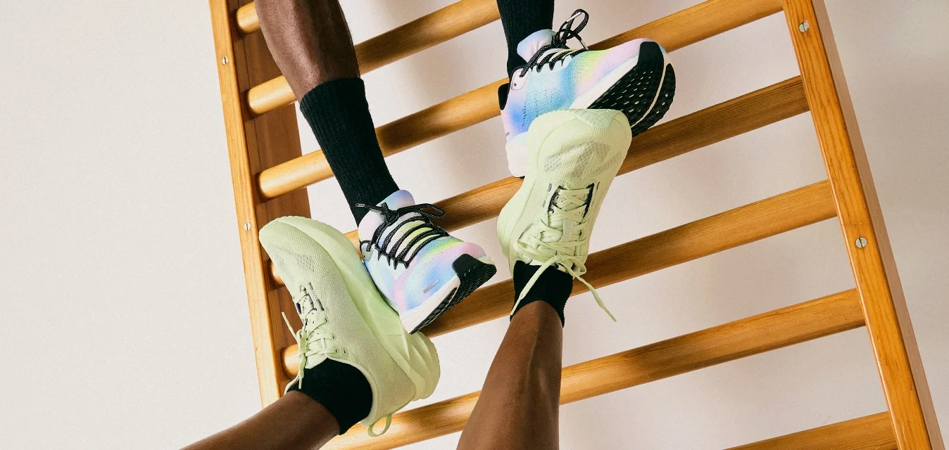 Due persone che indossano scarpe da ginnastica e calzini neri interagiscono con una scala di legno contro un muro bianco semplice.