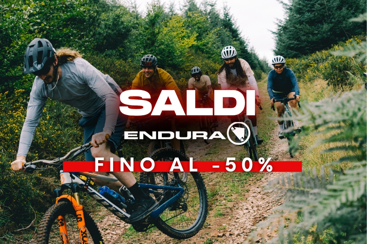 Group of mountain bikers on a forest trail with a red 'SALDI Endura fino al -50%' banner advertising up to 50% off cycling gear