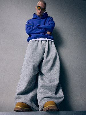 Uomo con felpa blu con cappuccio e pantaloni grigi molto larghi.