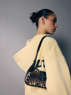 Donna con felpa giallo chiaro con cappuccio e borsa a fantasia sulla spalla.