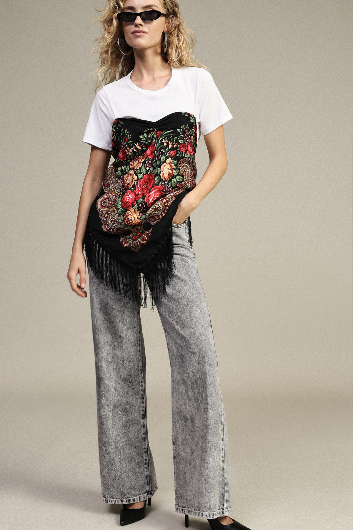 Woman wearing white T-shirt layered with black floral fringed scarf top, grey wide-leg jeans and sunglasses