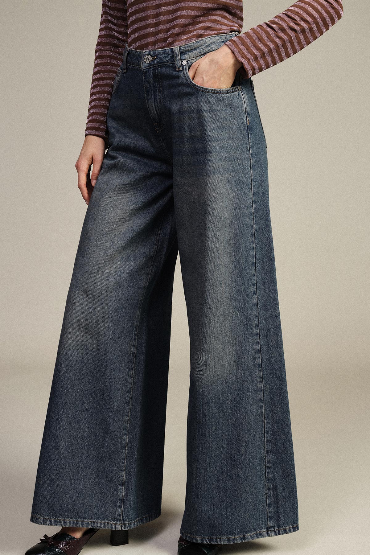 Woman wearing high-waisted wide-leg dark blue denim jeans with hand in pocket, paired with striped long-sleeve top and black heels