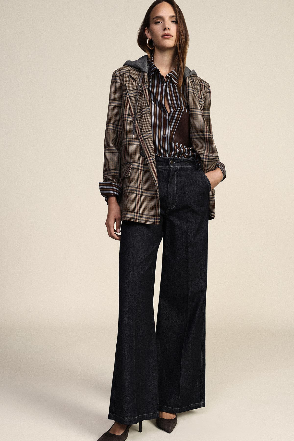 Woman modelling checked blazer, striped blouse, wide-leg dark jeans and heels, standing with one hand in pocket