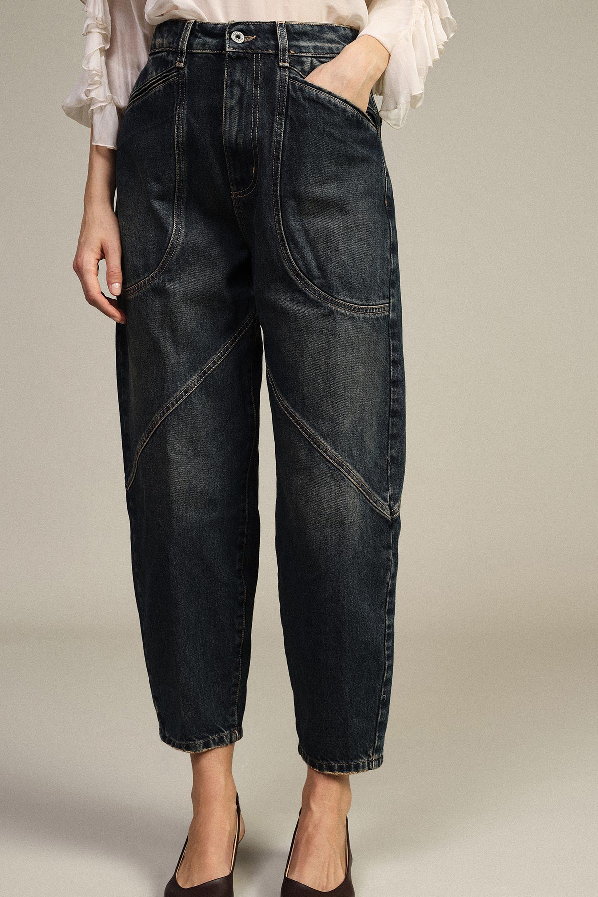 Cropped shot of model wearing high‑waisted dark wash tapered jeans with curved seam details, white blouse sleeves and heels