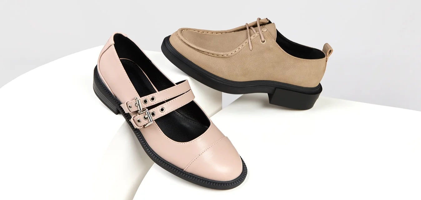 Scarpa in pelle rosa con doppia fascia e dettaglio della fibbia; scarpa in suede beige con design allacciato e suola in gomma nera. Entrambe su una superficie bianca.