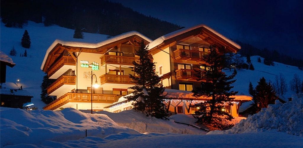 Alpine chalet-style hotel glowing at night, surrounded by deep snow and pine trees in a tranquil winter mountain setting