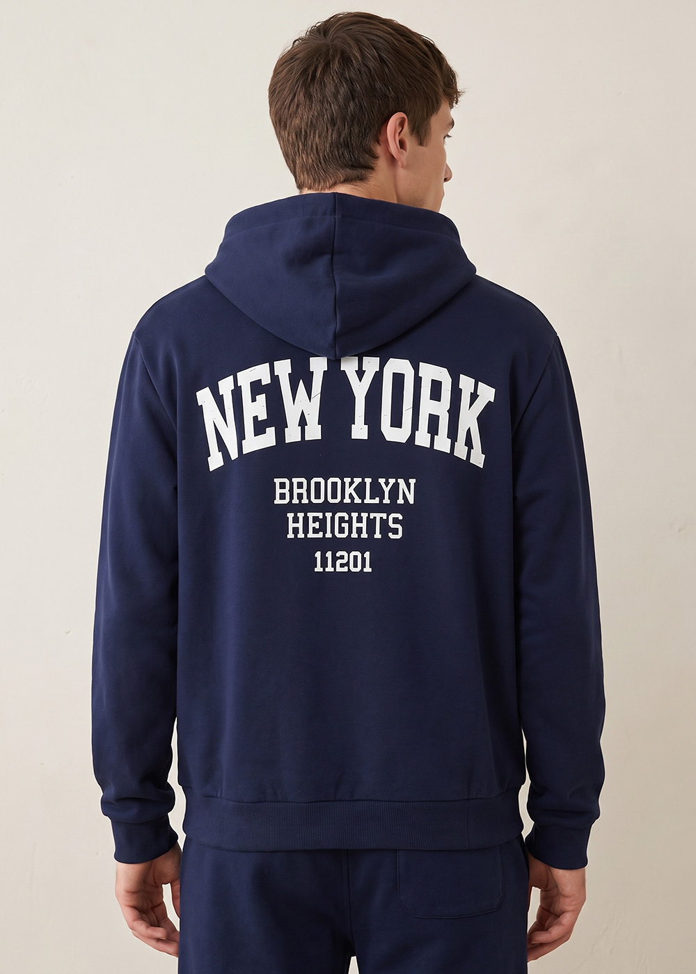 Rear view of man wearing navy hoodie with white 'NEW YORK BROOKLYN HEIGHTS 11201' print, casual outfit