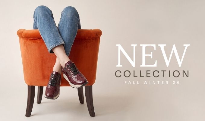 Person seated in orange velvet armchair wearing blue jeans and burgundy leather sneakers, promotional 'New Collection Fall Winter 26' text