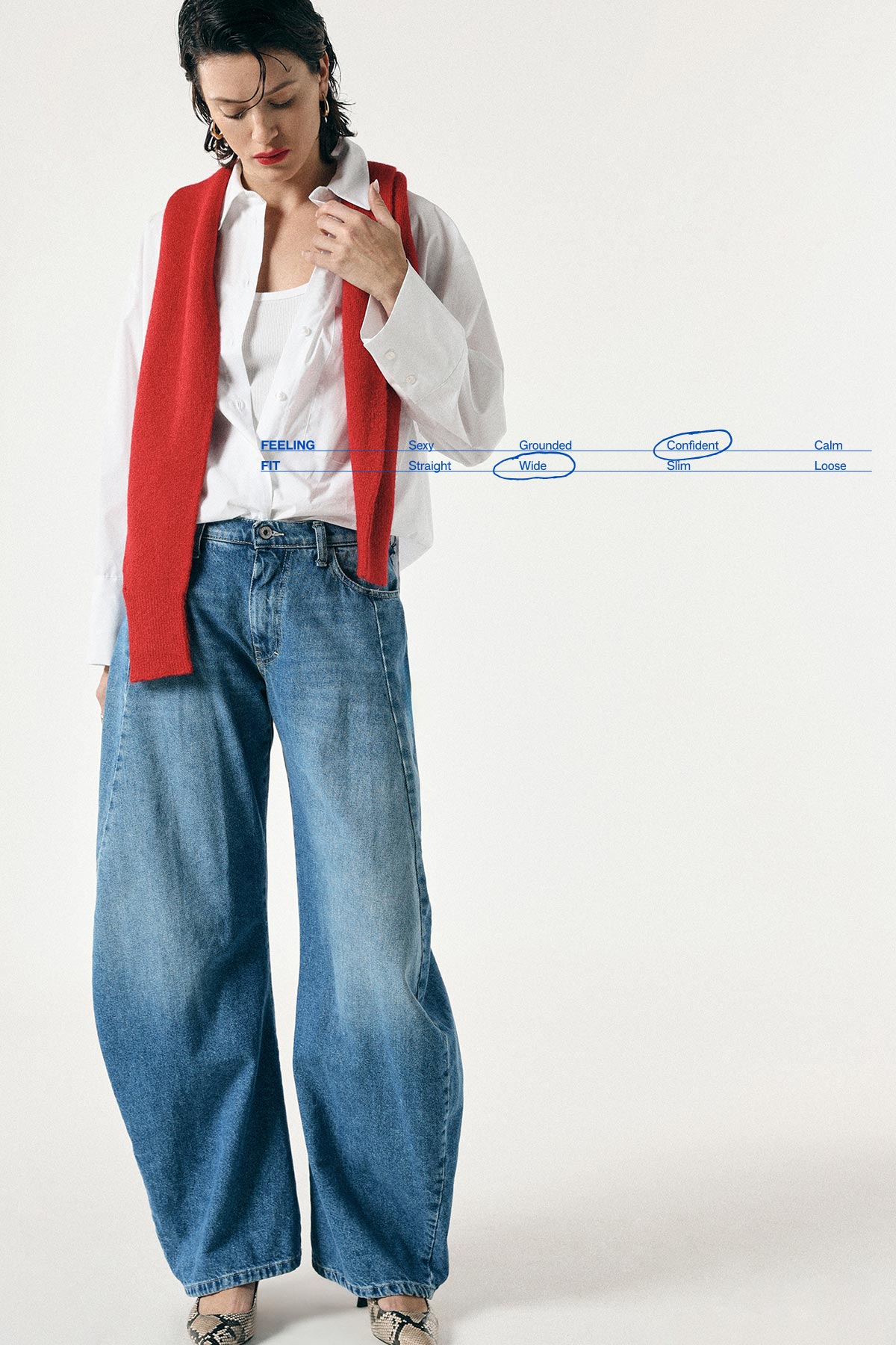 Woman modelling a casual outfit: white shirt with red sweater draped over shoulders and loose wide-leg blue jeans, looking down