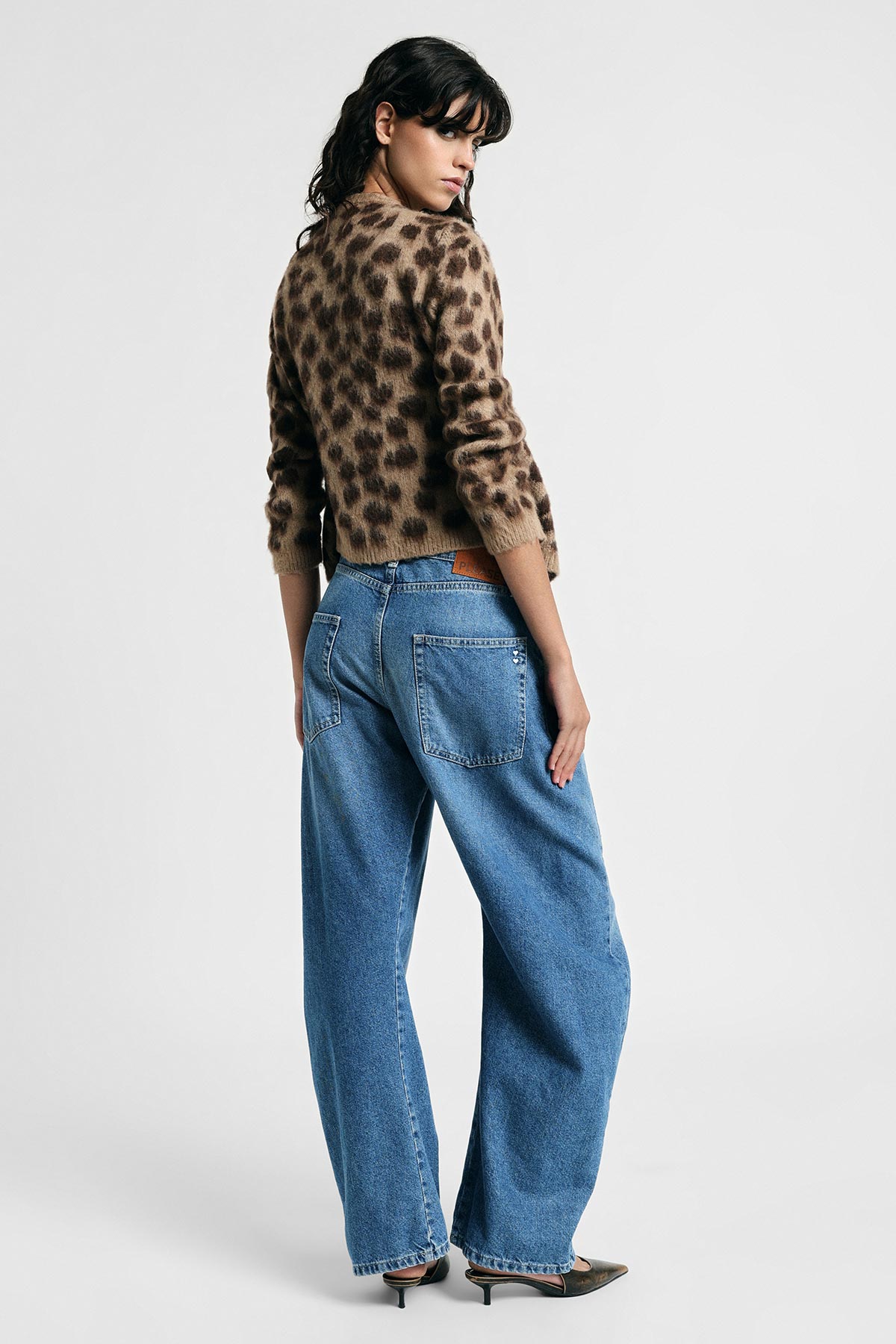 Woman modelling leopard-print sweater and high-waist wide-leg blue jeans, looking over her shoulder while wearing pointed heels