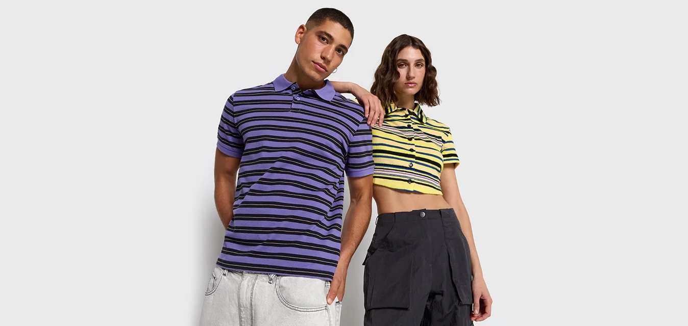 Due persone indossano polo a righe; il maschio in viola e nero e la femmina in giallo e nero. Entrambi gli abiti hanno maniche corte e una vestibilità casual.