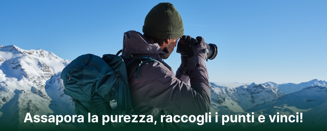 Escursionista con zaino che fotografa il paesaggio delle montagne innevate, con il testo Assapora la purezza, raccogli i punti e vinci!