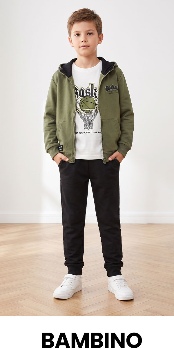 Boy in olive zip hoodie, graphic white T-shirt, black joggers and white trainers standing on a wooden floor