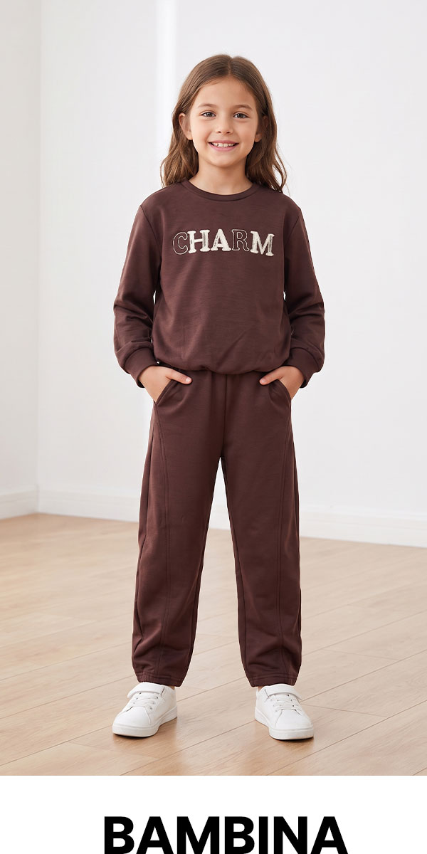 Smiling girl in brown 'CHARM' sweatshirt and matching joggers, hands in pockets, white trainers, standing against a neutral studio background