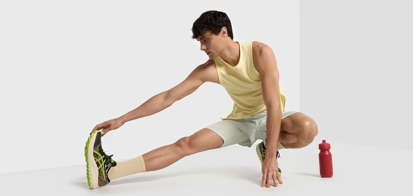 Completo sportivo composto da una maglietta gialla senza maniche, pantaloni corti verde chiaro e scarpe da corsa nero-verdi, con una bottiglia d'acqua rossa accanto.