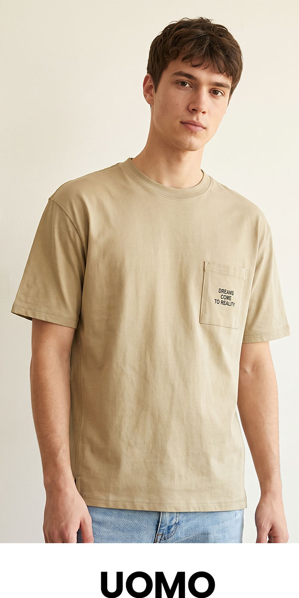 Young man wearing beige pocket T-shirt with 'Dreams Come To Reality' print, casual light-wash jeans, neutral studio background