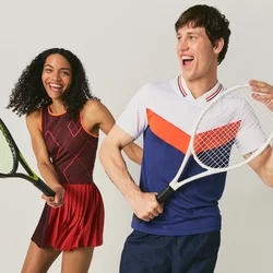 Un uomo e una donna sorridenti in abbigliamento da tennis posano con racchette, in piedi davanti a uno sfondo chiaro e semplice.