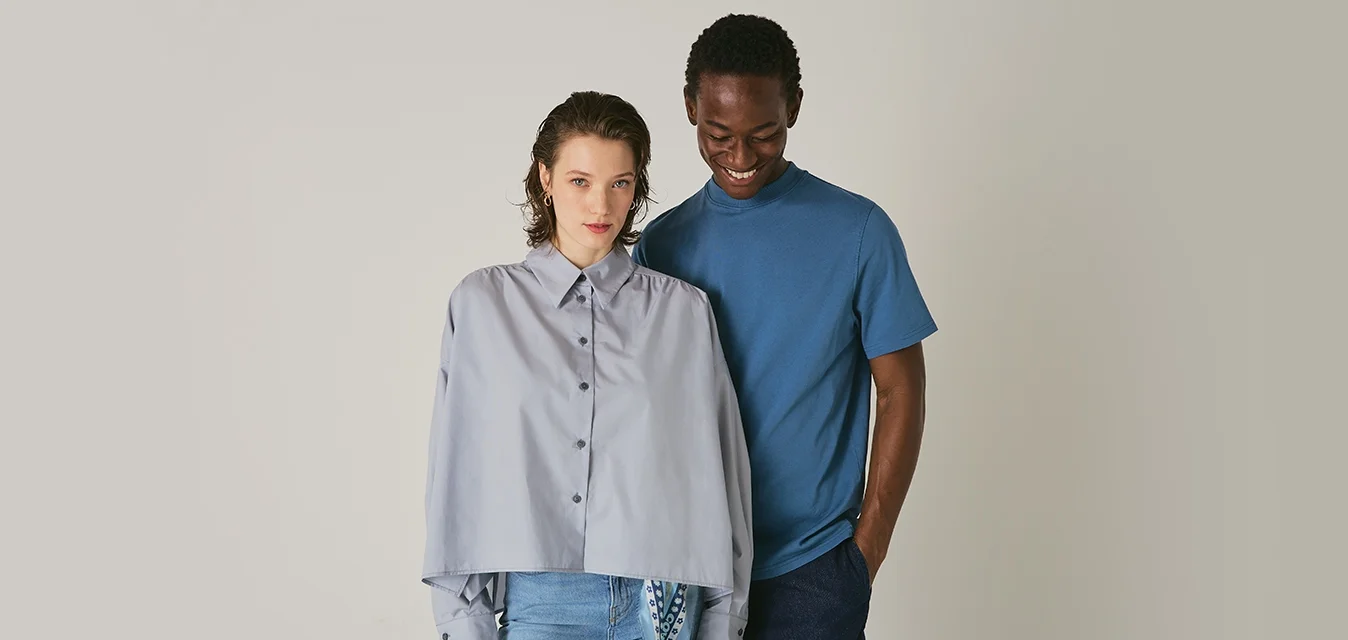 Camicia grigia chiaro con maniche oversize abbinata a una maglietta blu; entrambi presentano stili casual su uno sfondo neutro.