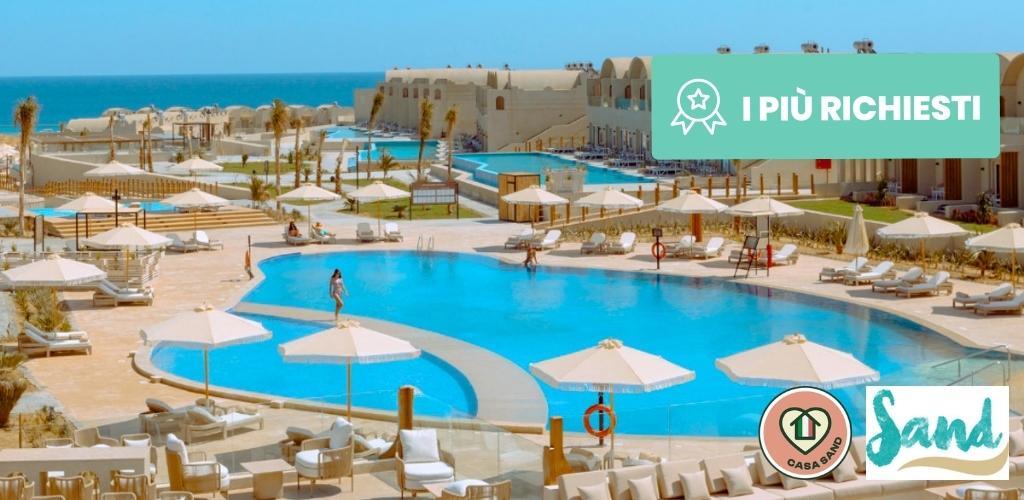 Coastal resort with large curved outdoor pool, sun loungers and parasols on a sun-drenched terrace overlooking the turquoise sea