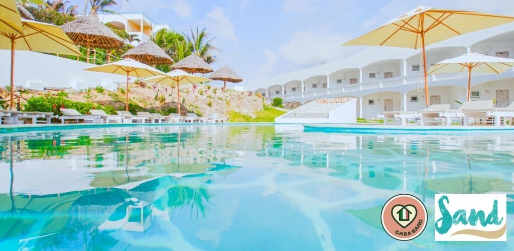 Resort infinity pool with turquoise water, sun-loungers and yellow parasols beside white beachfront bungalows and palm trees