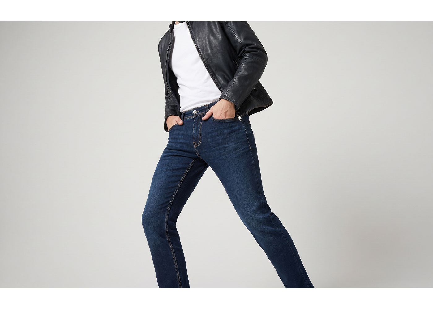 Person wearing a black leather jacket, white t-shirt and dark blue slim jeans with hands in pockets and a wide stance
