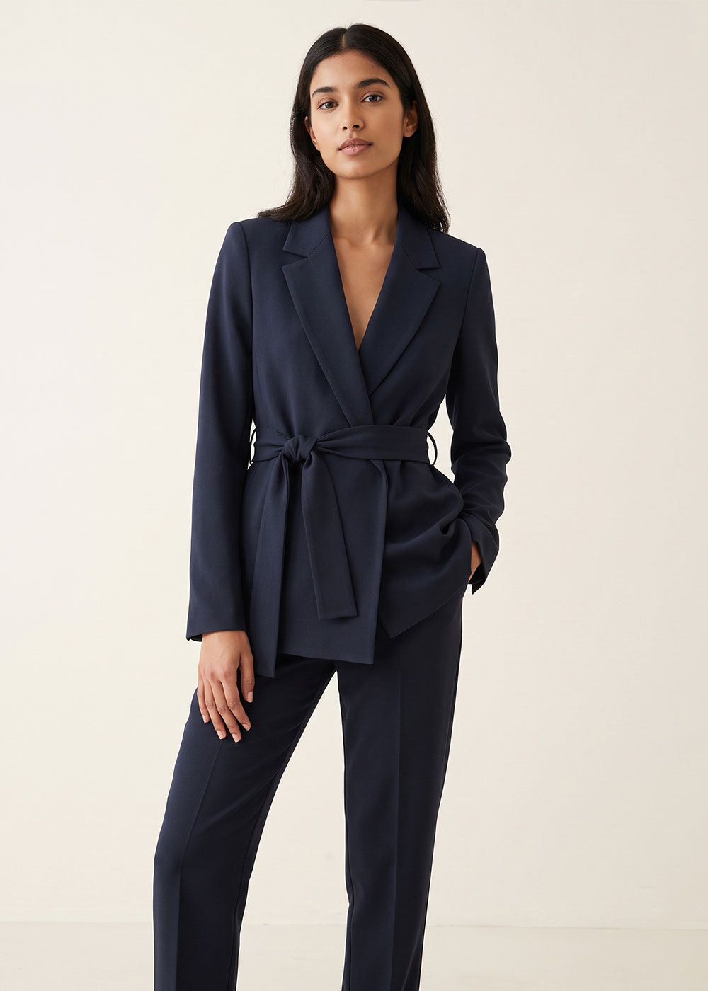 Woman modelling navy belted blazer with matching tailored trousers on a plain background — women's business‑casual suit
