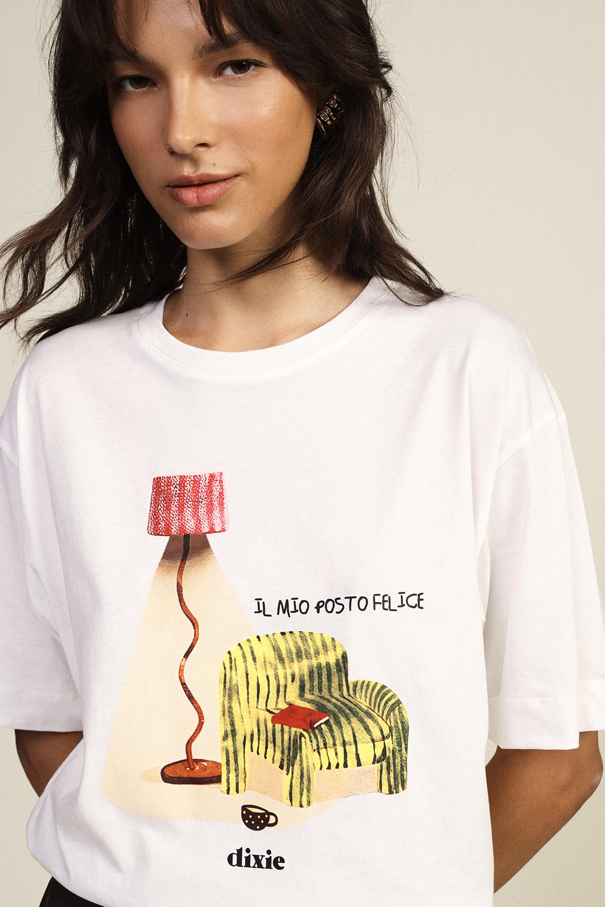 Woman wearing white T-shirt with printed armchair and floor lamp illustration, text 'Il mio posto felice' and 'dixie' logo