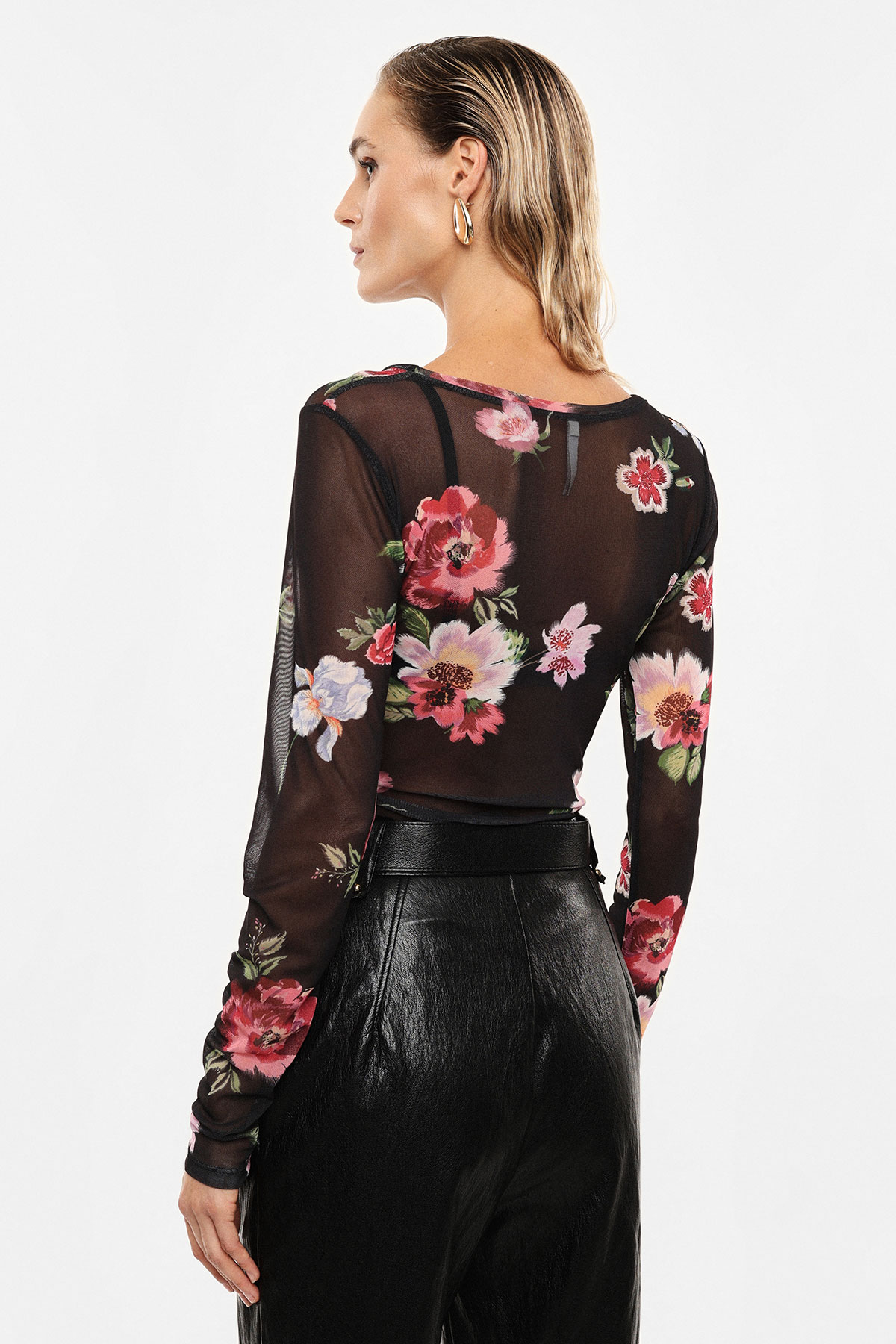 Rear view of woman wearing a sheer black floral long-sleeve top and high-waisted black leather trousers with gold hoop earrings