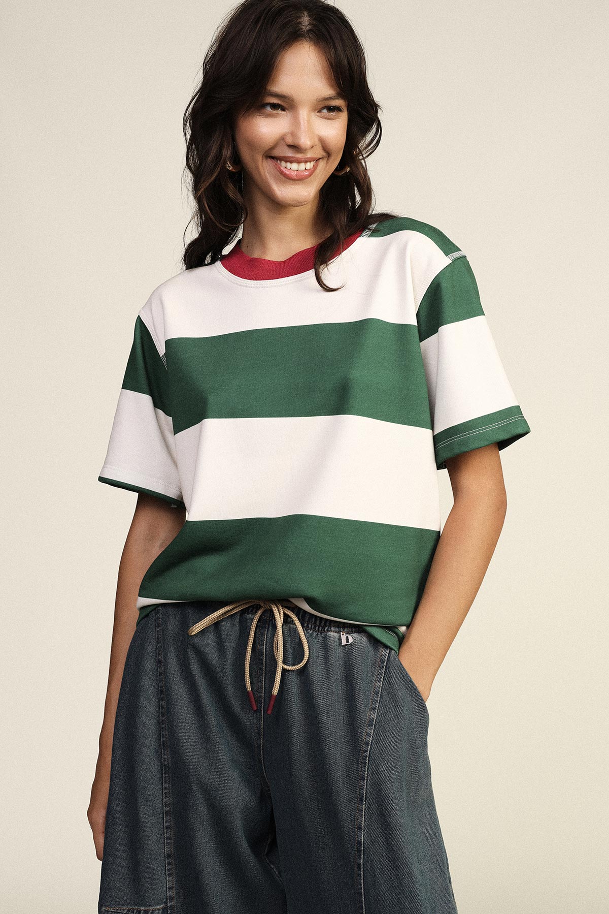 Smiling woman wearing green and white striped T-shirt with red collar and denim drawstring trousers, hand in pocket