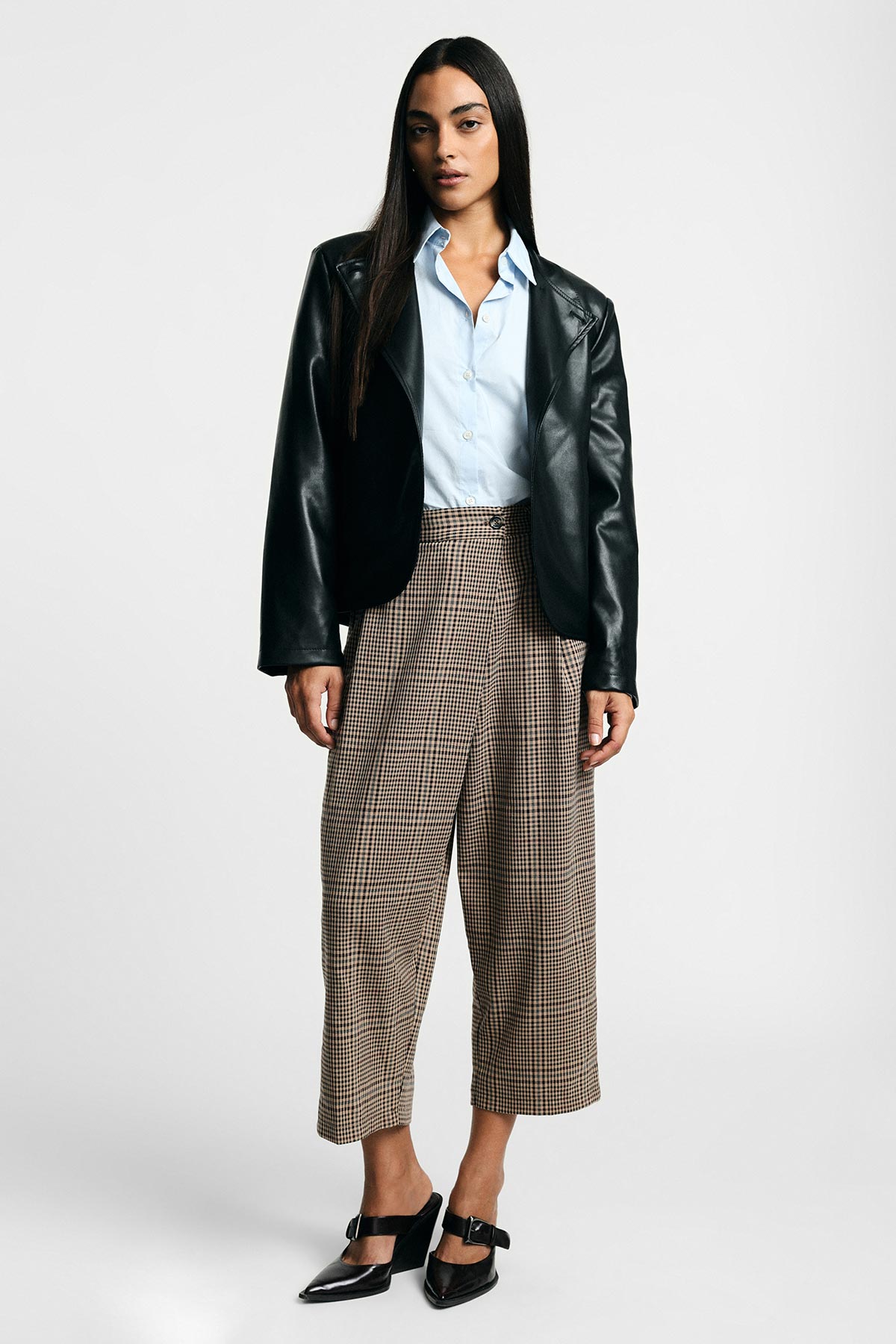 Female model standing in black leather blazer, light blue shirt, checked cropped wide-leg trousers and black buckle heels