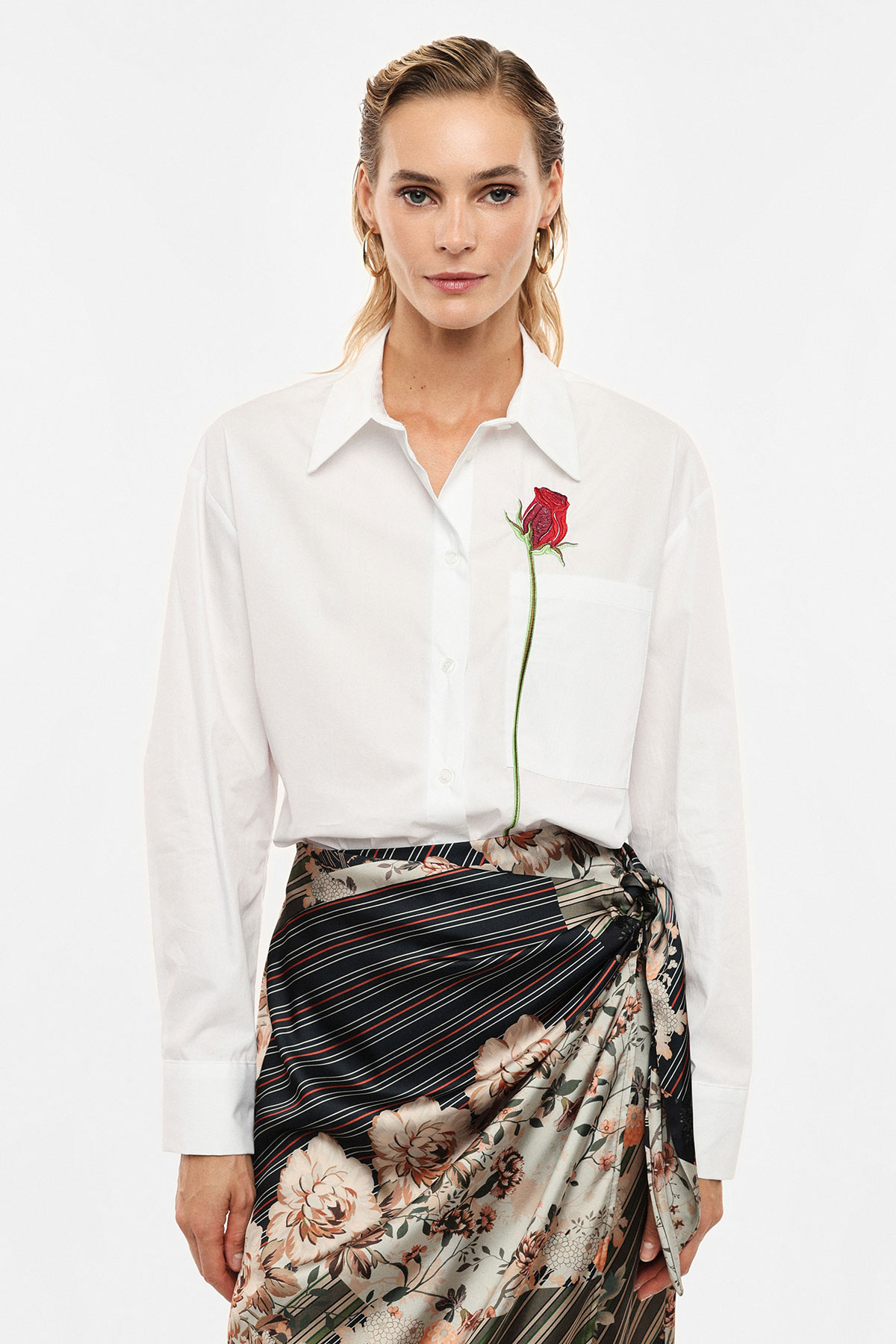 Woman modelling white button-down shirt with embroidered red rose on chest and floral patterned wrap skirt, fashion outfit