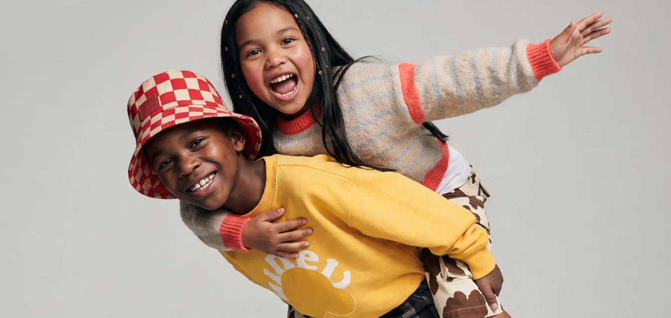 Due bambini sorridenti, uno che porta l'altro in spalla; uno indossa una felpa gialla e un cappello a quadri rossi.