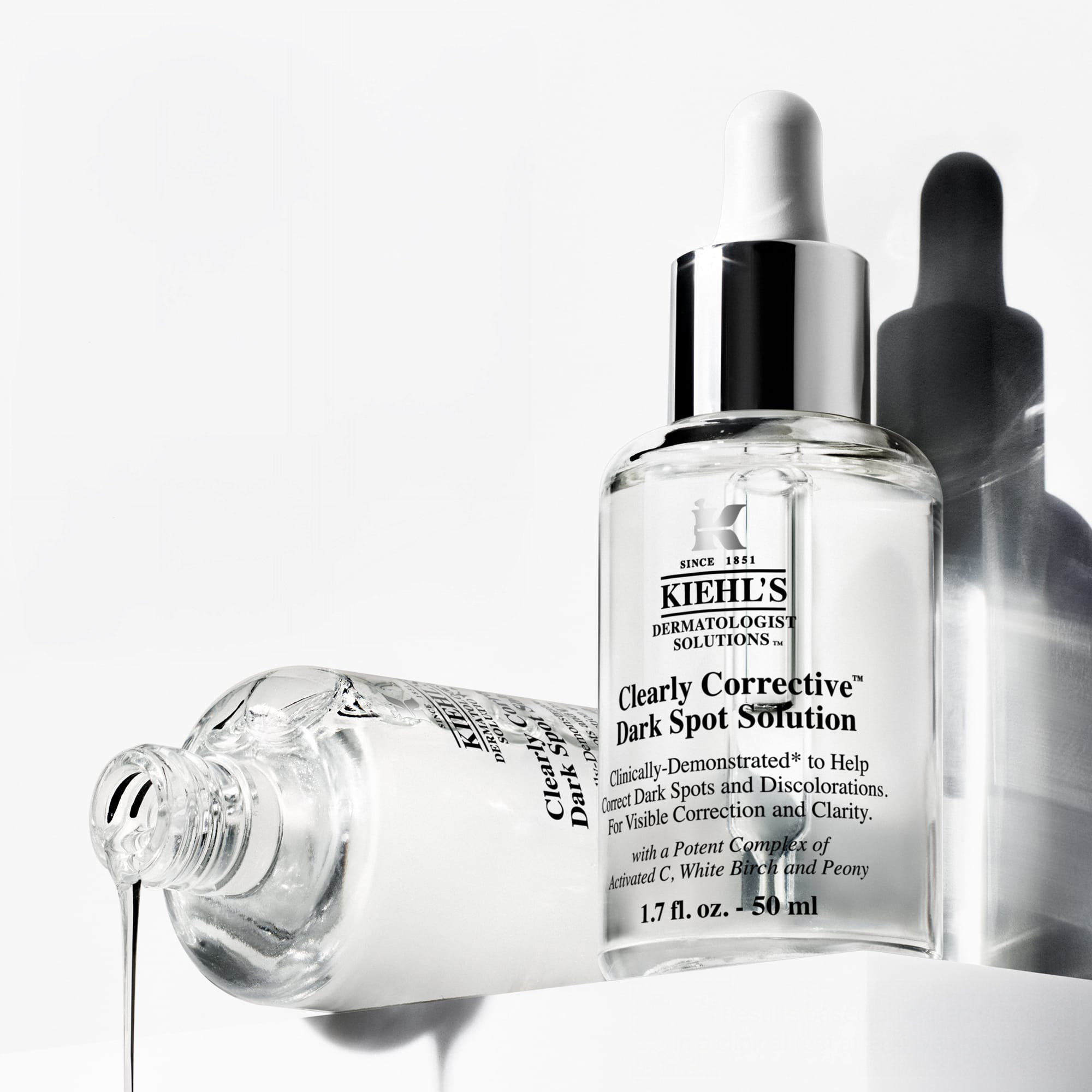 Flacone contagocce Kiehl's Clearly Corrective Dark Spot Solution accanto a siero che fuoriesce da una boccetta aperta
