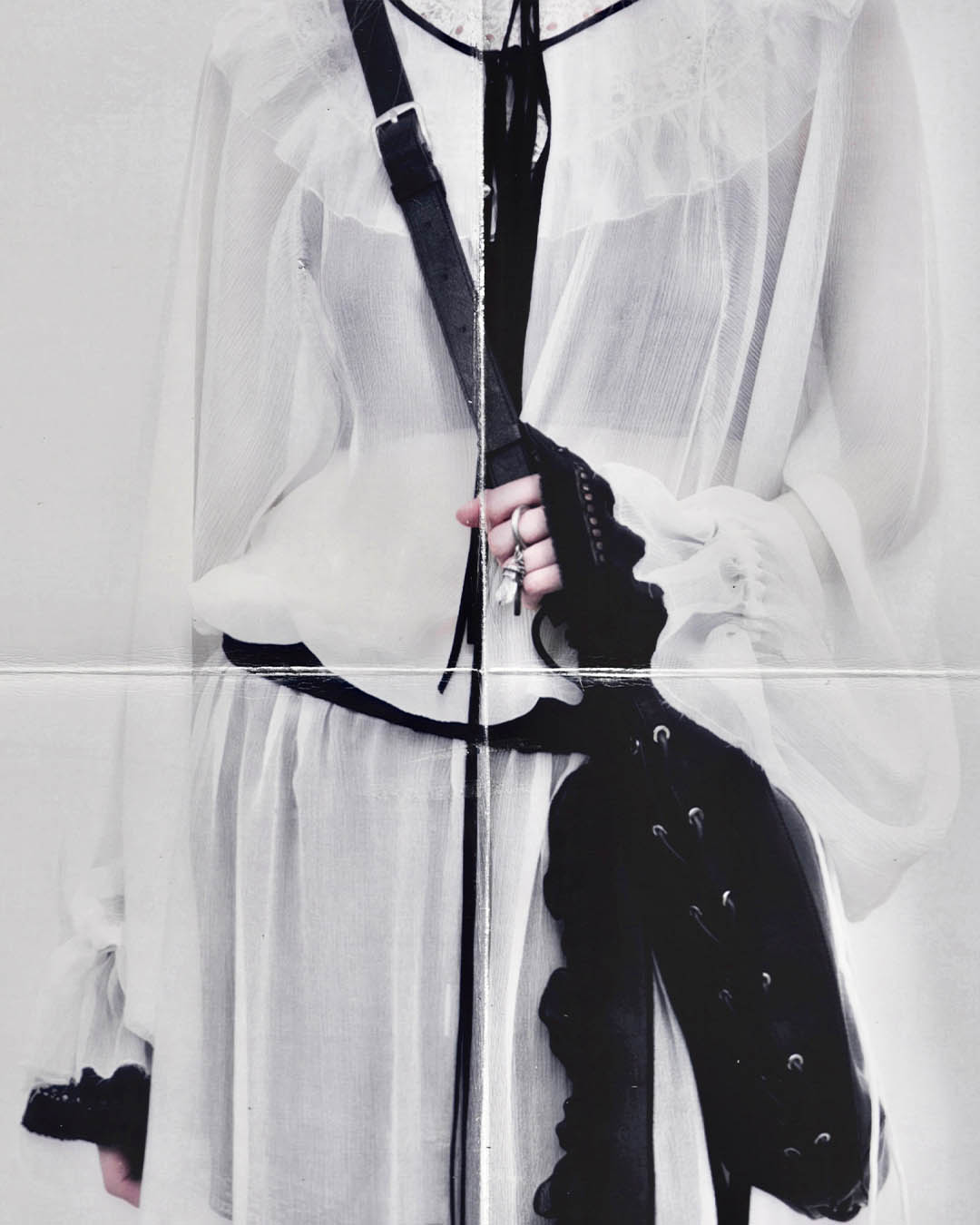 Close-up of person wearing sheer white Victorian-style blouse and skirt, black leather crossbody bag and hand with silver rings