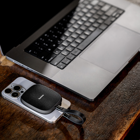 L'SSD del telefono SanDisk collegato allo smartphone si trova su una scrivania di legno accanto a un laptop