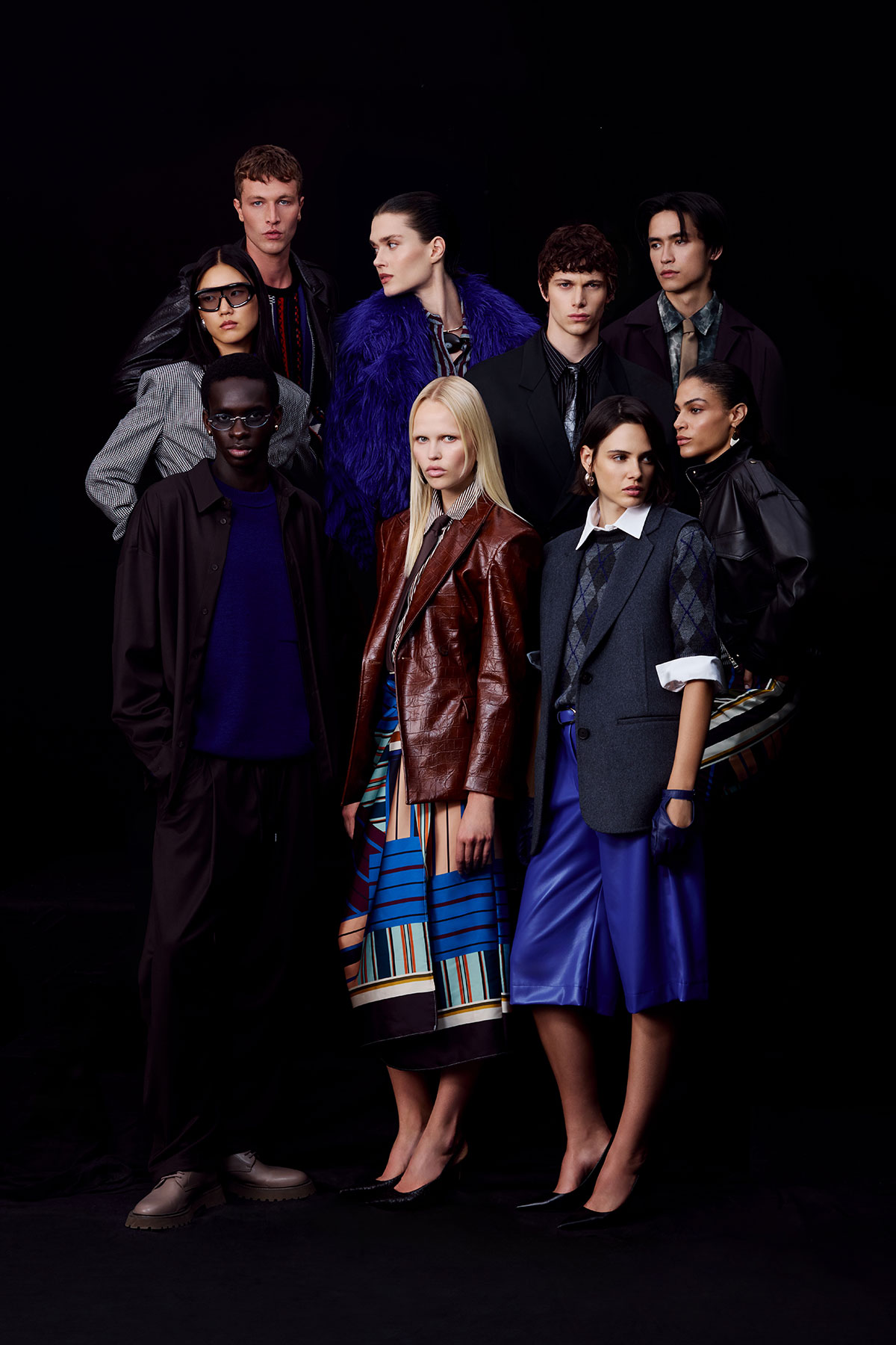 Diverse group of fashion models in layered autumn/winter outfits and mixed textures posing against a dark studio backdrop