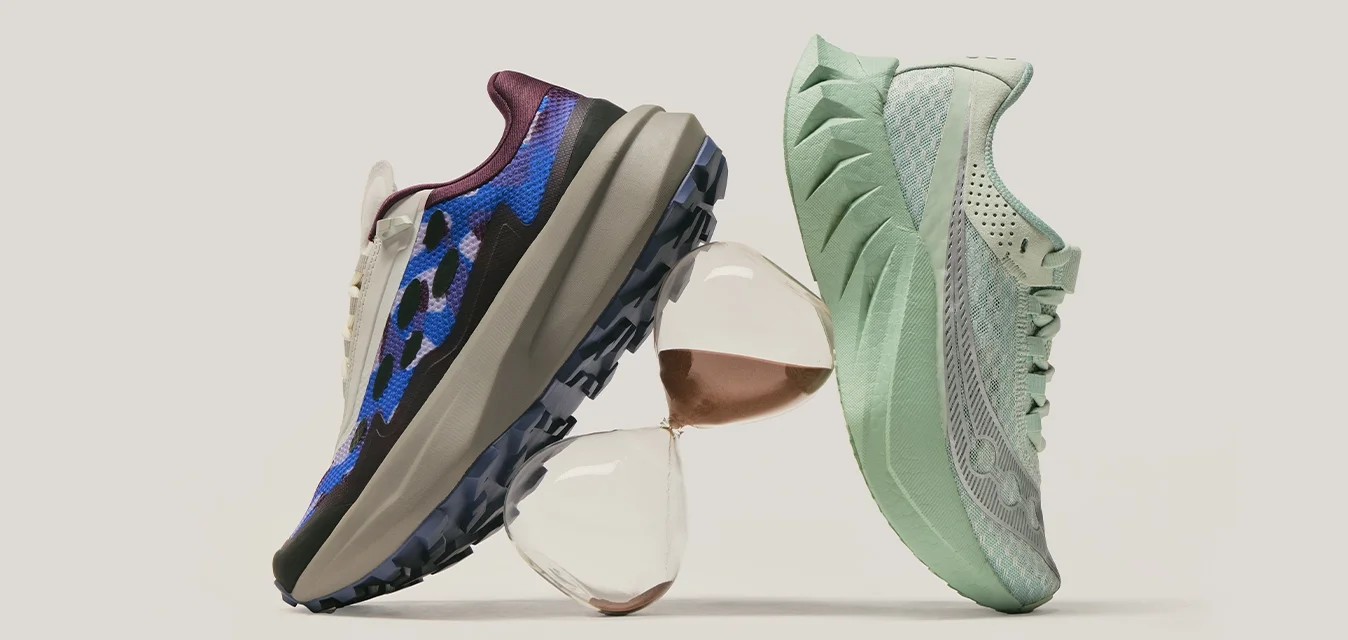 Due scarpe da ginnastica, una blu con motivo mimetico e una verde chiaro, equilibrate su oggetti di vetro impilati contro uno sfondo semplice.