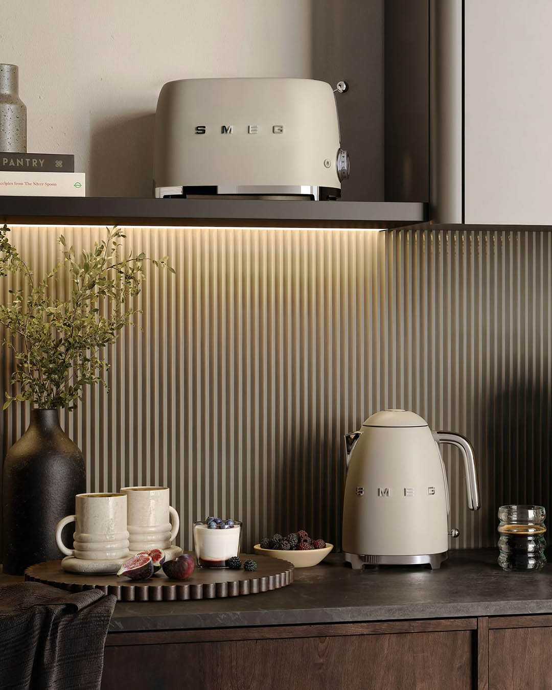 Beige SMEG kettle and toaster on dark kitchen counter with ceramic mugs, berries, a vase and fluted metallic backsplash