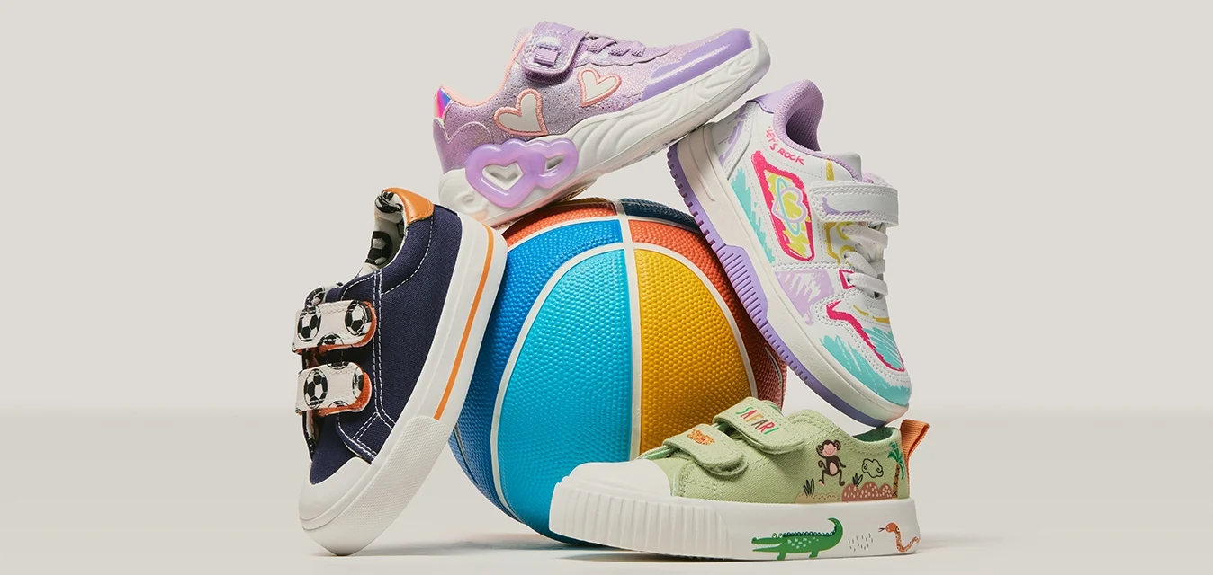 Quattro scarpe colorate per bambini impilate intorno a una palla blu, gialla e arancione su uno sfondo semplice.