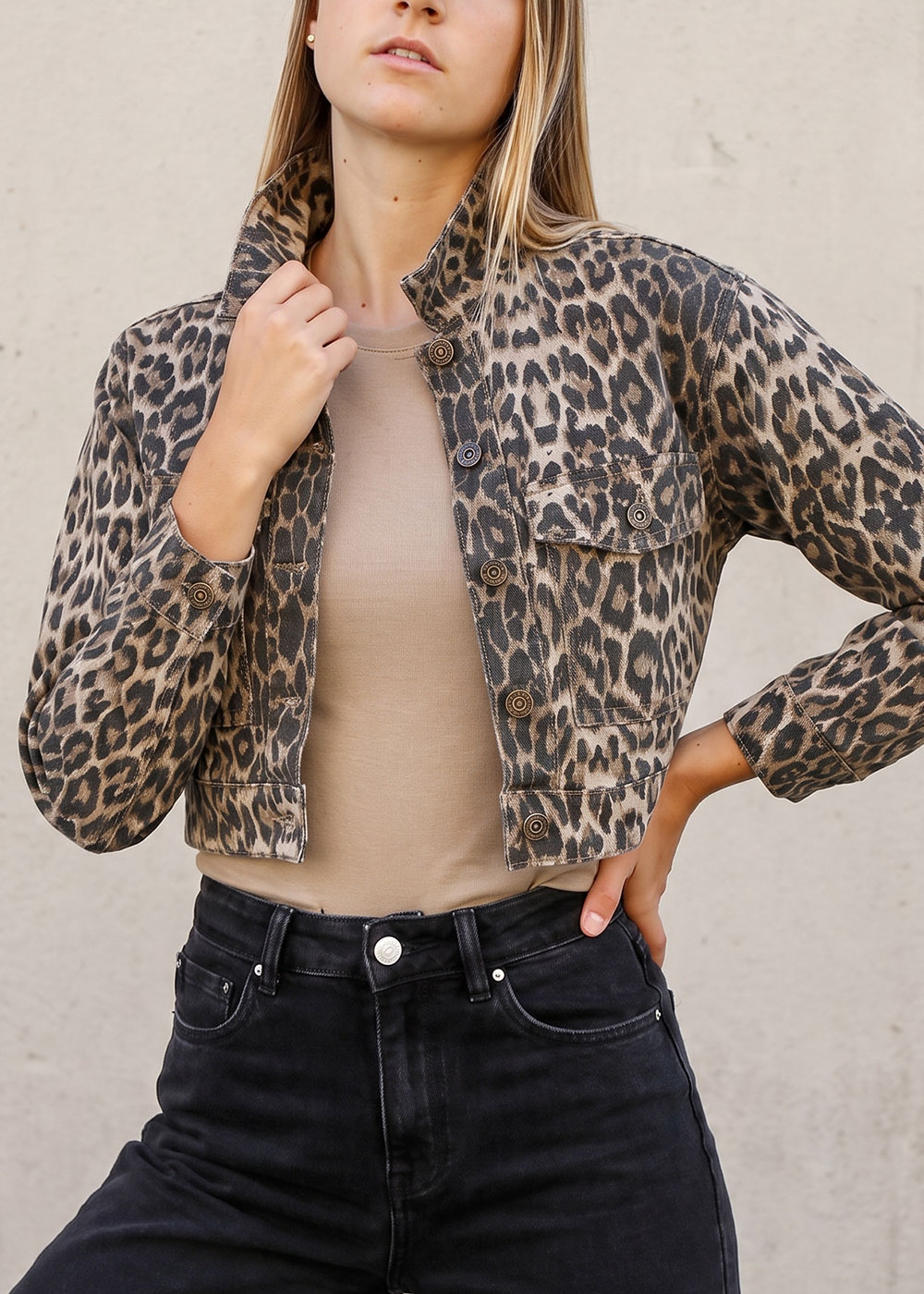Female model wearing leopard-print cropped jacket over beige top paired with high-waist black jeans, hand on hip