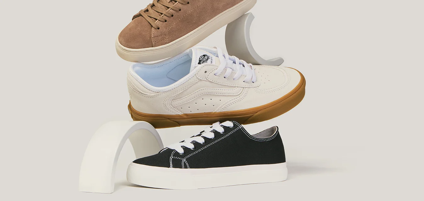 Tre sneaker casual marroni, bianche con accenti blu e nere impilate verticalmente su supporti curvi bianchi.