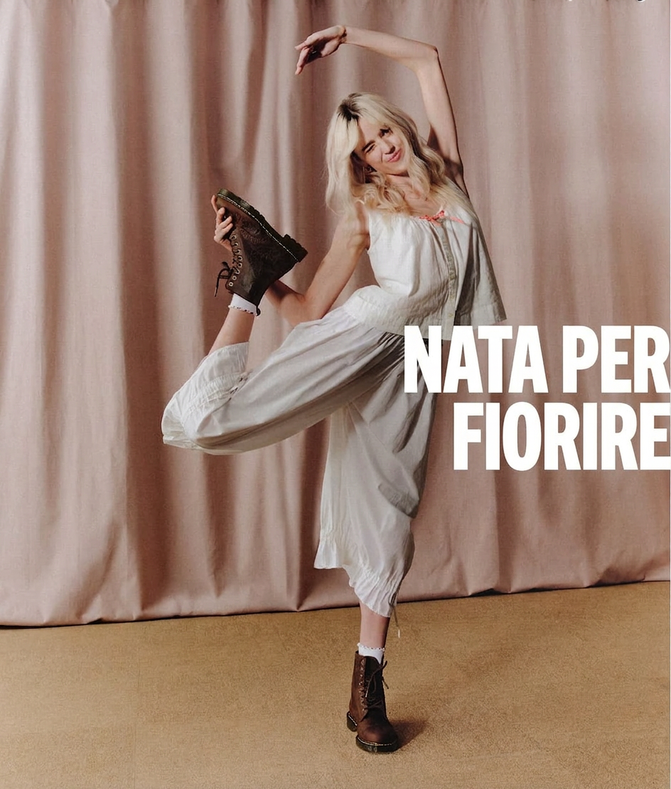 Woman in white outfit and brown boots strikes a pose with text "NATA PER FIORIRE".