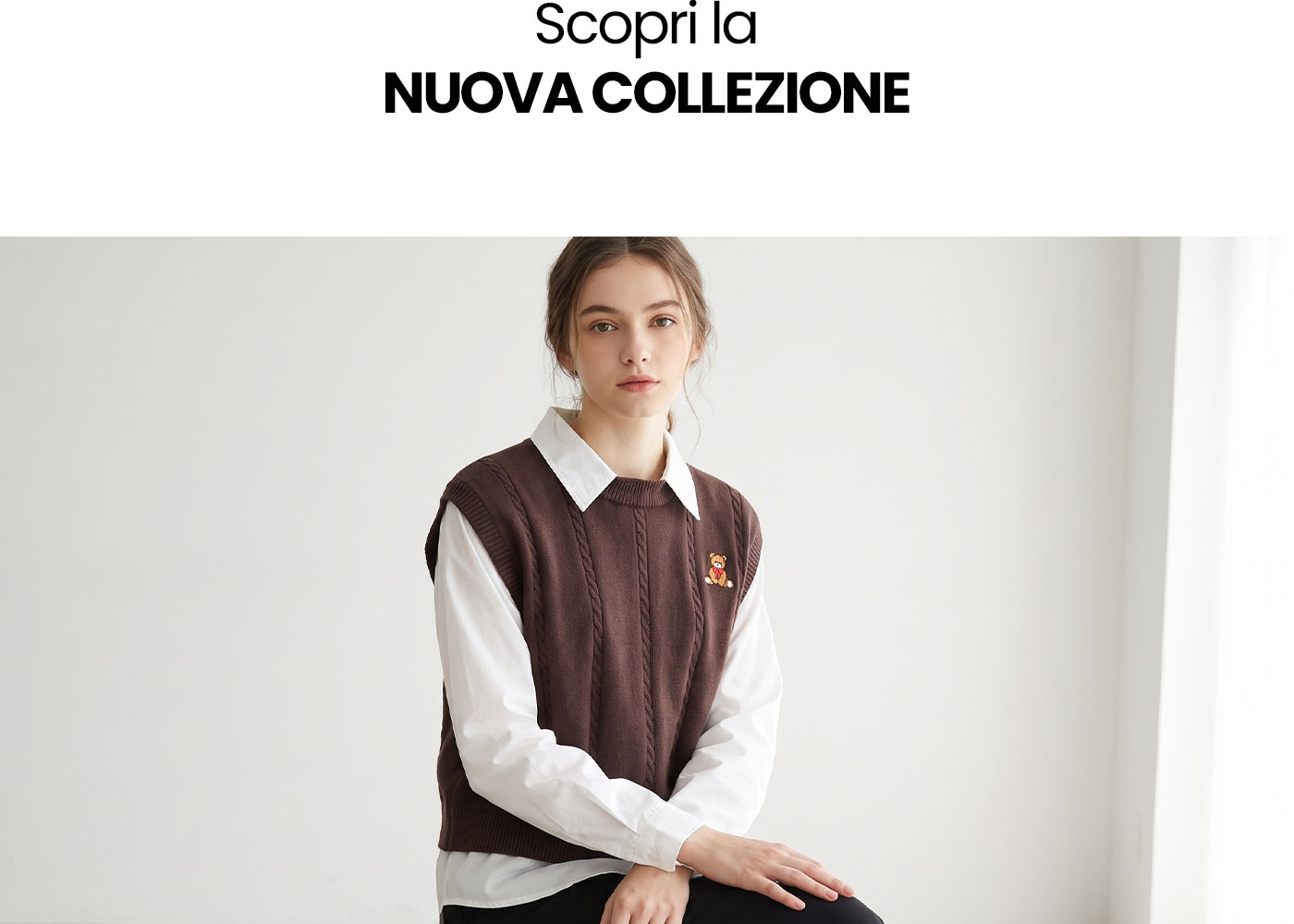 Model wearing brown cable-knit sleeveless jumper over white shirt, seated against pale background – new collection