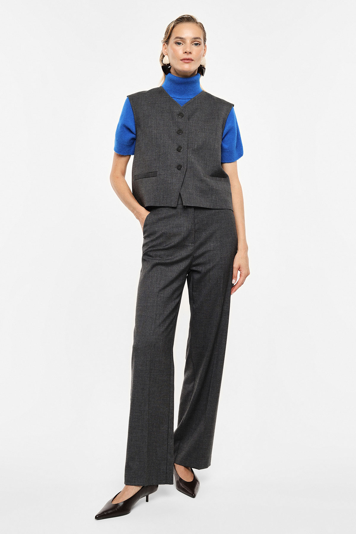 Woman modelling grey tailored waistcoat and matching trousers with blue short-sleeve roll-neck and black heels