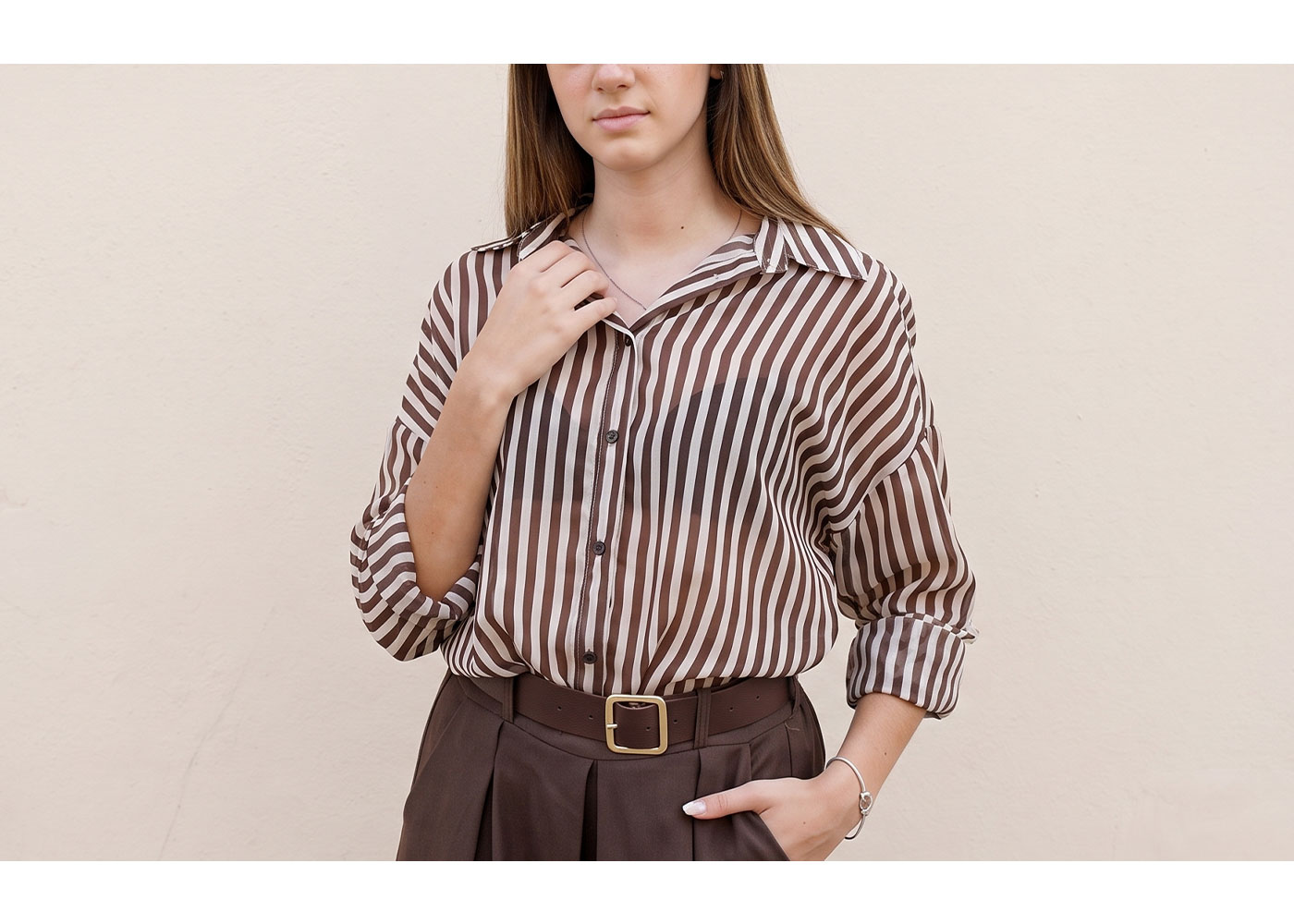 Woman wearing brown and white vertical striped blouse tucked into high-waisted brown trousers with belt, hand on collar