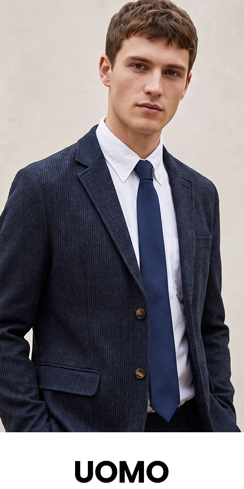 Male model wearing navy pinstripe blazer, white shirt and navy tie against a neutral background with UOMO logo