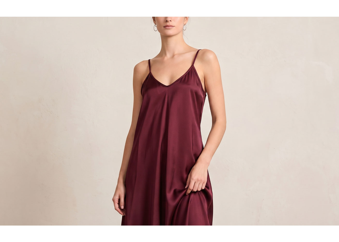 Woman modelling burgundy satin slip dress with thin spaghetti straps against a neutral background