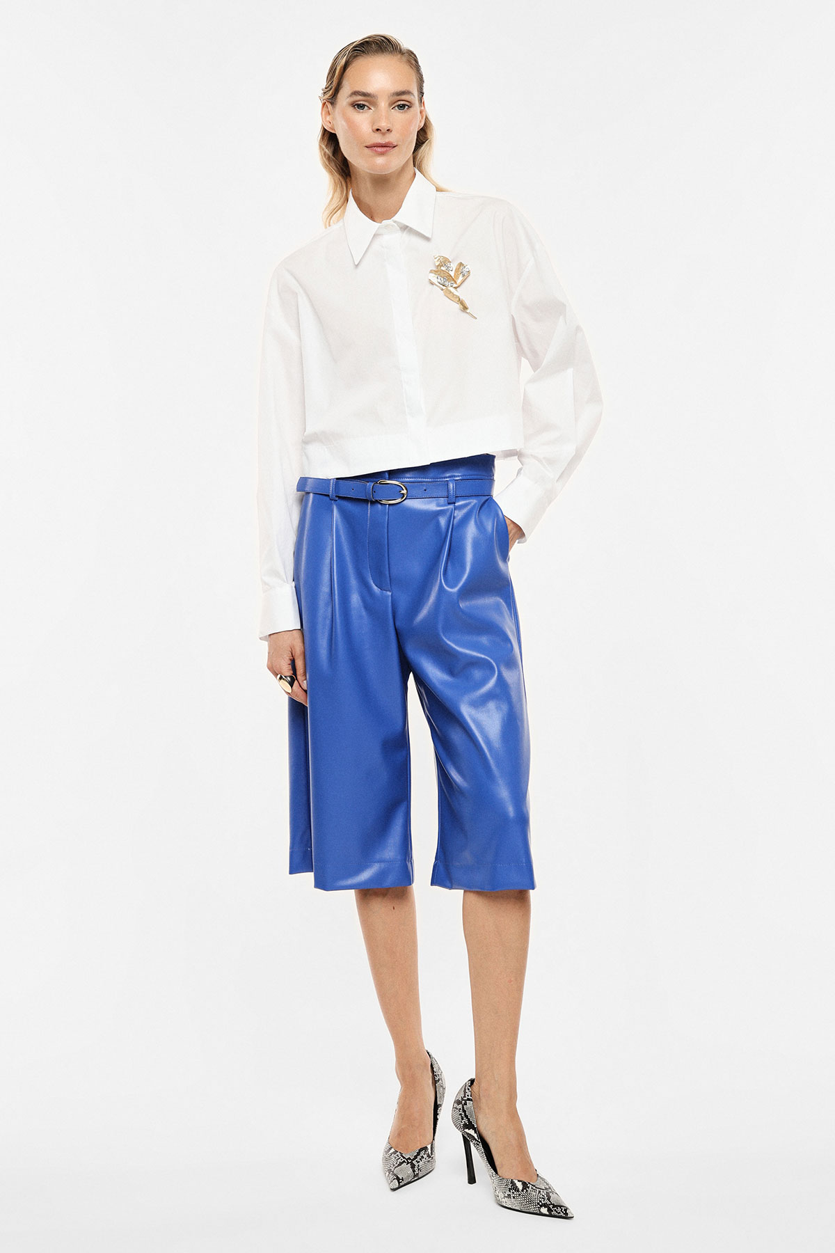Woman modelling white cropped shirt with embroidery and blue leather knee-length culottes, belted, with snakeskin heels